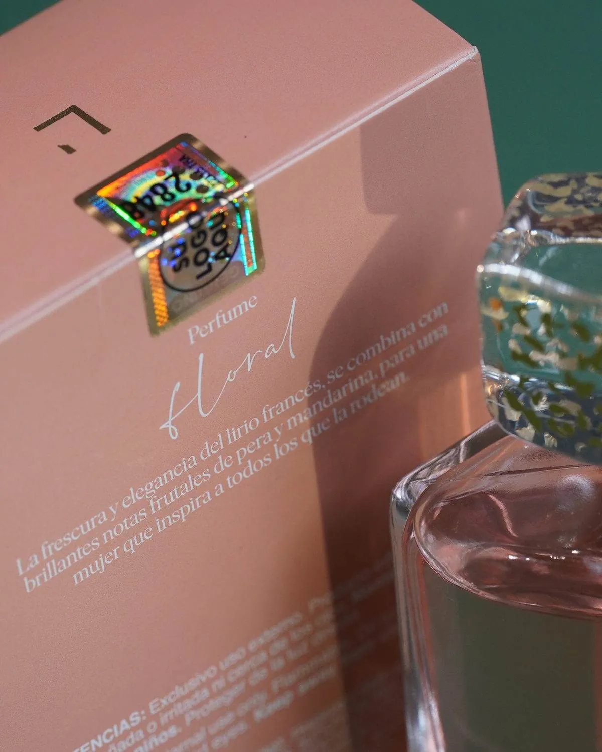 Estuche de perfume sellado con un holograma dorado numerado, junto al frasco del producto