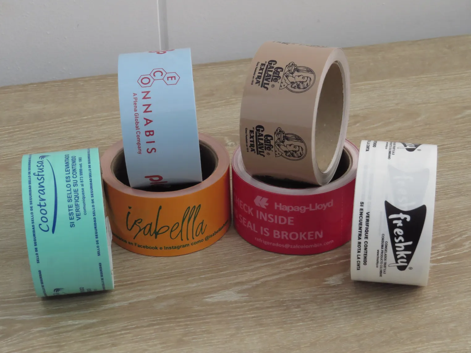 Rollos de cinta de precinto en varios colores, cada uno con la marca impresa de su cliente