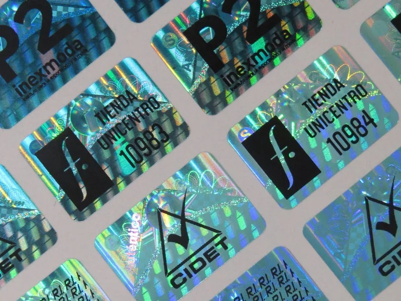 Detalle de hologramas personalizados en tono turquesa con logos distintos y numeración