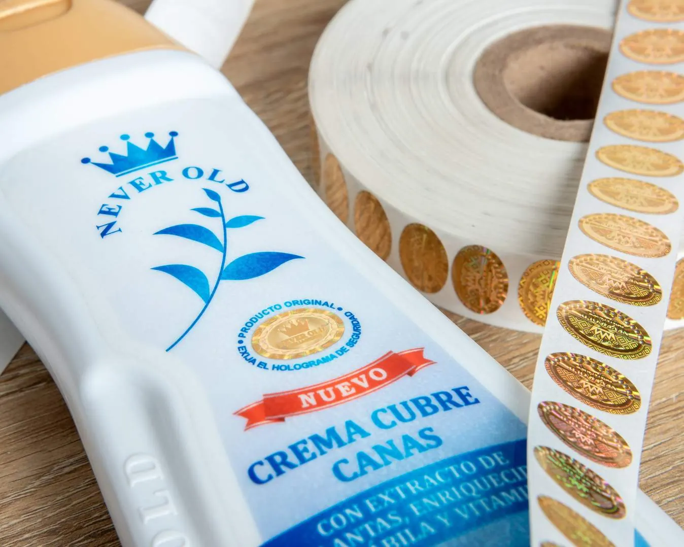 Envase de crema con sello holográfico de autenticidad junto a un rollo de hologramas dorados
